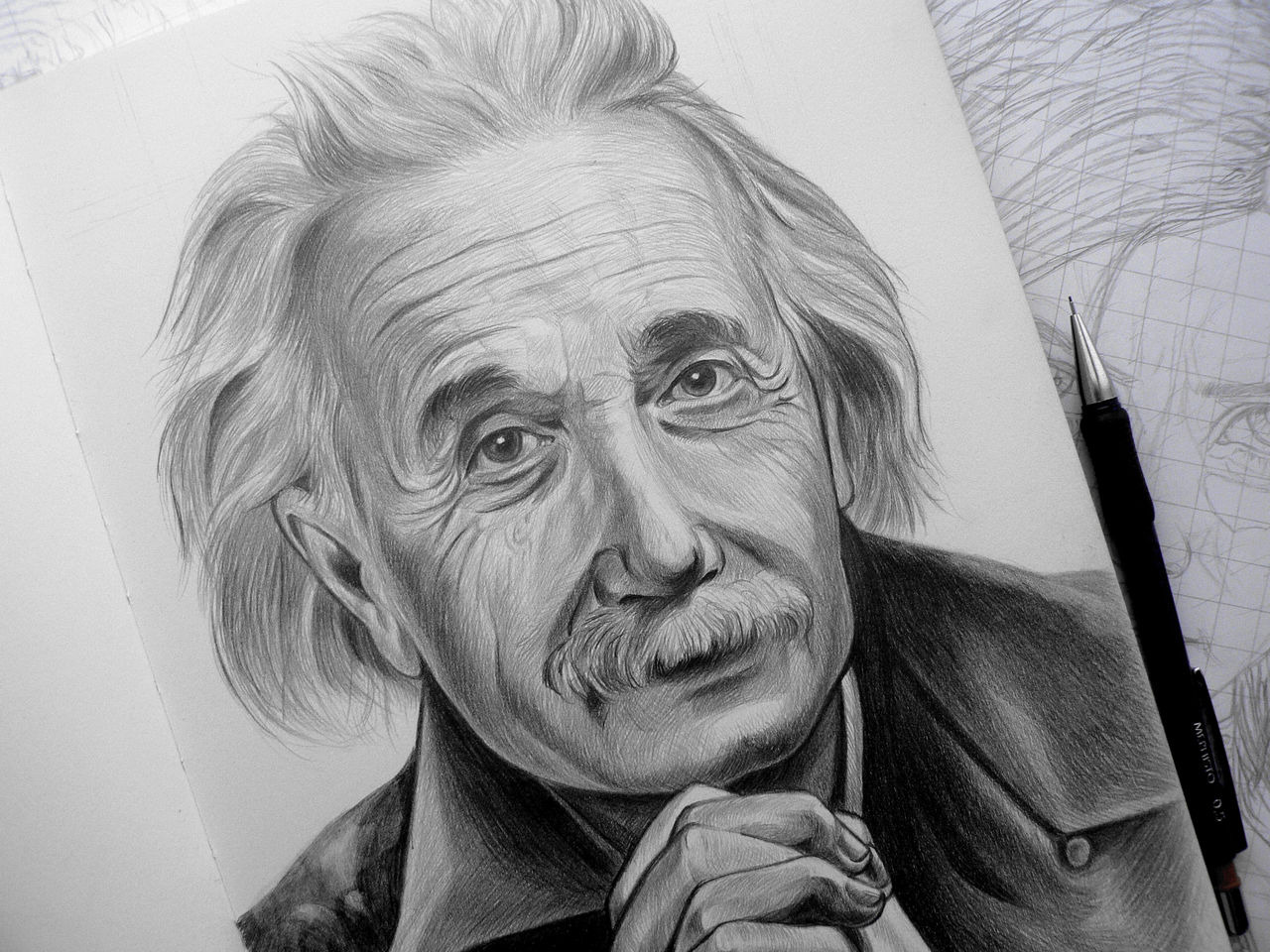 Realistyczny portret ołówkiem Alberta Einsteina. Widoczne detale twarzy, faktura skóry i włosów. Obok leży ołówek automatyczny. Tło stanowi szkicownik.