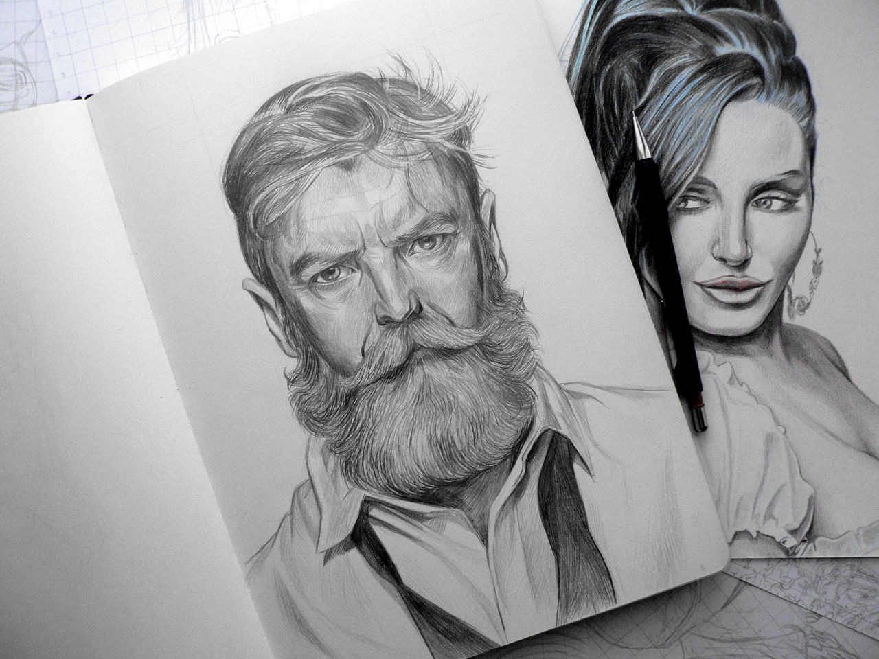 Szkic ołówkiem: portret brodatego mężczyzny w otwartym szkicowniku, obok portret kobiety. Ołówek leży na szkicach. Detaliczna kreska, silne światło.