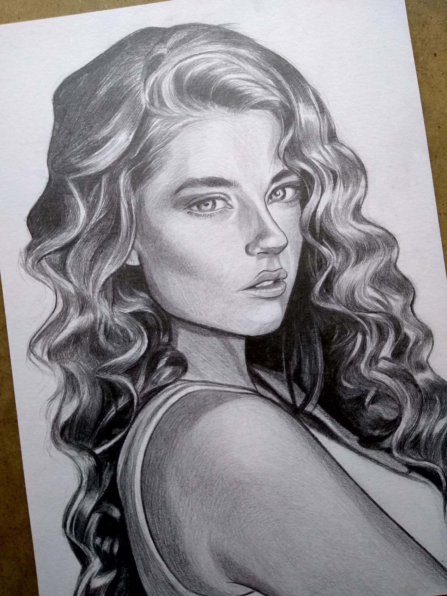 Realistyczny portret kobiety z kręconymi włosami, wykonany ołówkiem na białym papierze. Widoczny detaliczny rysunek twarzy i miękkie cieniowanie.