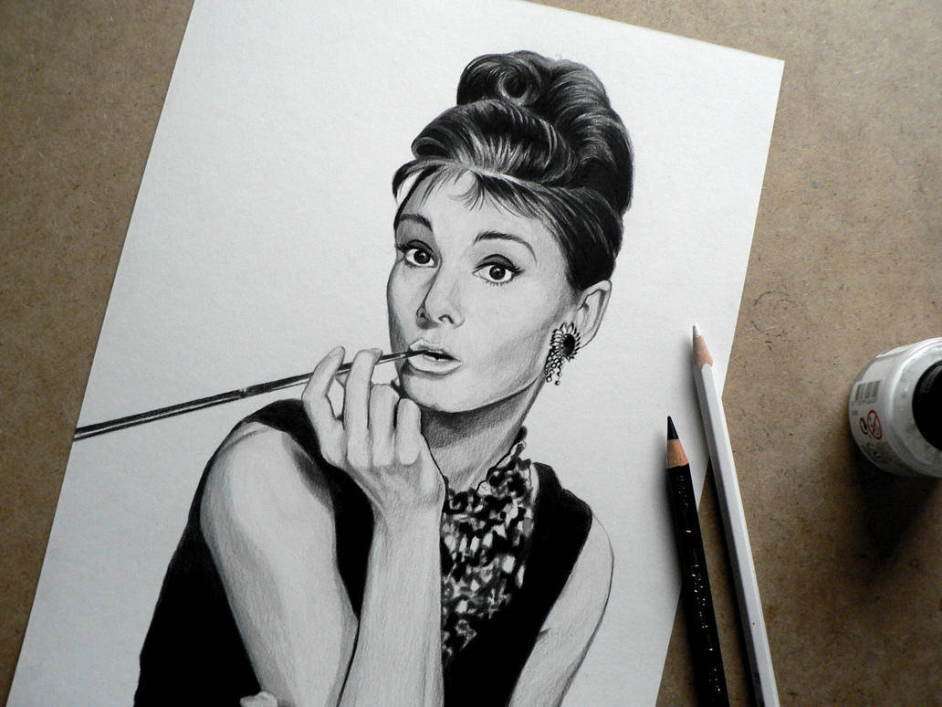 Realistyczny portret ołówkiem Audrey Hepburn z papierosem, obok leżą dwa ołówki i pojemnik z tuszem. Detaliczne cieniowanie, elegancki styl.