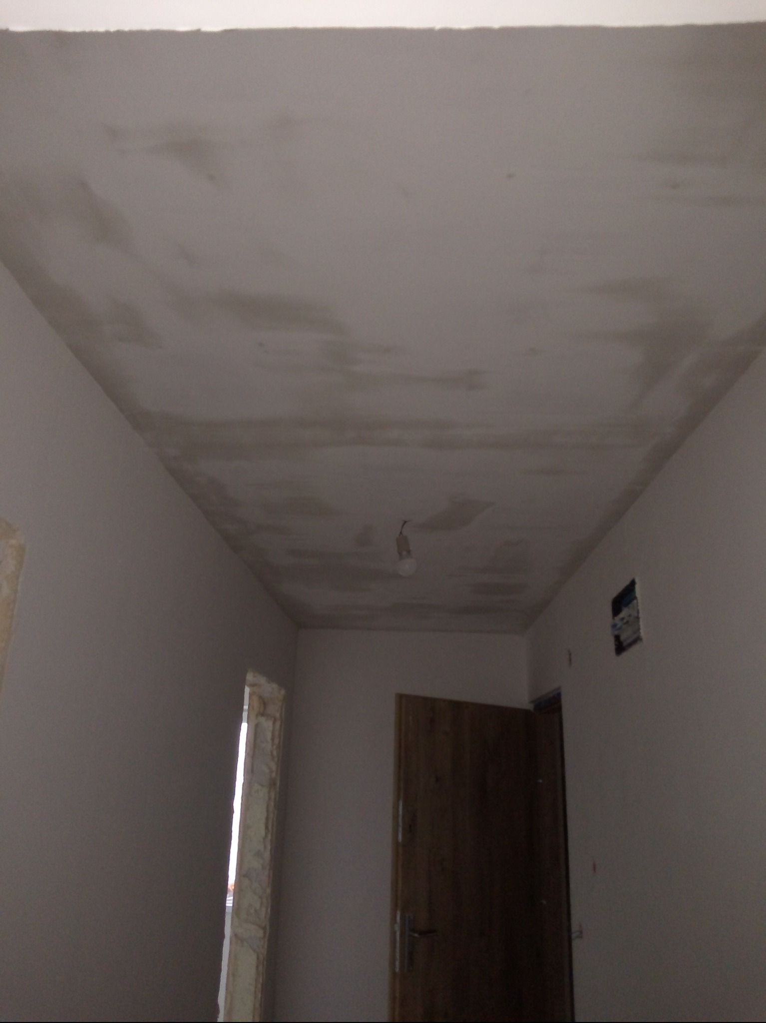 Niedokończone gładzie na suficie w trakcie remontu mieszkania. Widoczne ślady po szpachlowaniu i przygotowaniu do malowania. W tle drzwi i fragment ściany.