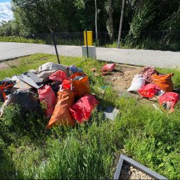 Zgarnę To - Duża ilość odpadów budowlanych, w tym styropian w pomarańczowych i czerwonych workach, leżąca na trawniku przy chodniku z kostki brukowej, obok czarnego ogrodzenia.
