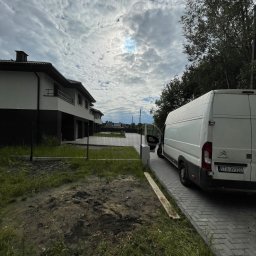 Zgarnę To - Biały dostawczy Citroen z otwartymi drzwiami bocznymi, zaparkowany na kostce brukowej przed szeregiem nowoczesnych domów. W tle zachmurzone niebo, na pierwszym planie trawnik i ziemia.