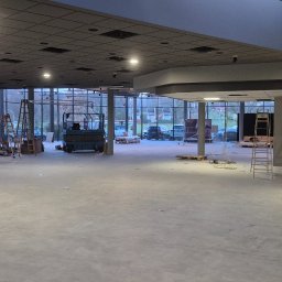 Michał Murdza - Wnętrze komercyjne w trakcie prac wykończeniowych: nowa posadzka, drabiny, podnośnik nożycowy, duże okna. Widoczne przygotowania do dalszych prac.