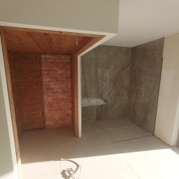 Michał Murdza - Łazienka w trakcie remontu: kabina prysznicowa z marmurowymi płytami, obok drewniana konstrukcja sauny w surowym stanie. Widoczne przewody na podłodze.