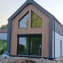 DREWLINE JAROSŁAW KISIELEWICZ - Nowoczesny dom z drewnianą elewacją i dużymi oknami, w trakcie wykończenia. Widoczne detale drewnianej fasady i otoczenie budynku.
