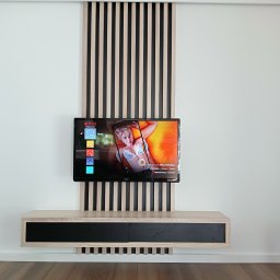 DREWLINE JAROSŁAW KISIELEWICZ - Nowoczesna ściana TV z drewnianymi lamelami w odcieniach beżu i czerni, podwieszana szafka RTV z czarnym frontem, drewniana podłoga. Minimalistyczny design.