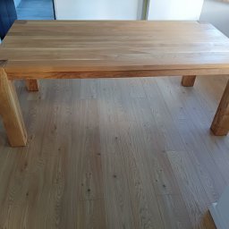 DREWLINE JAROSŁAW KISIELEWICZ - Solidny, jasny stół z drewna dębowego z grubym blatem i nogami, widoczny na tle drewnianej podłogi. Minimalistyczny design, naturalne wykończenie.