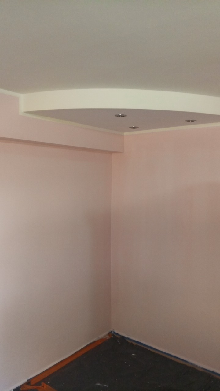 Pomalowane na różowo ściany pokoju z dekoracyjnym podwieszanym sufitem z oświetleniem punktowym. Podłoga zabezpieczona folią malarską.