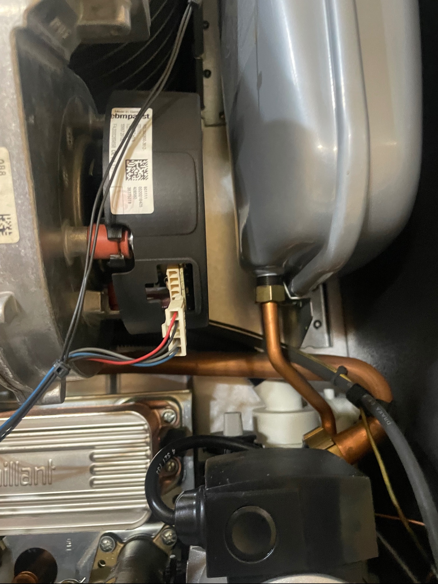 Wnętrze kotła gazowego marki Vaillant z widocznymi elementami instalacji, w tym miedzianymi rurami, czarną obudową i podłączeniem elektrycznym z kolorowymi przewodami.