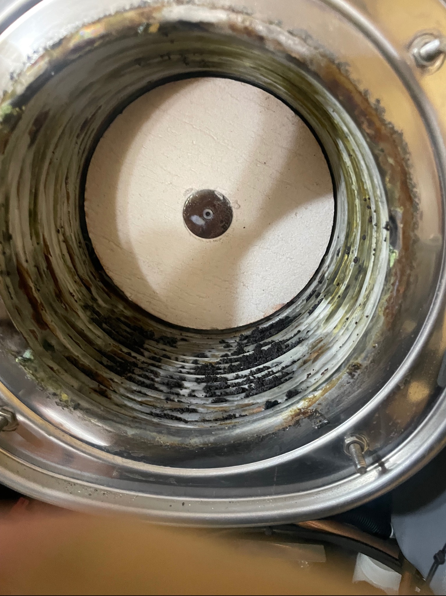 Wnętrze zanieczyszczonego, metalowego pieca gazowego z widocznymi osadami i zabrudzeniami. Centralnie umieszczony element ceramiczny z metalowym punktem.