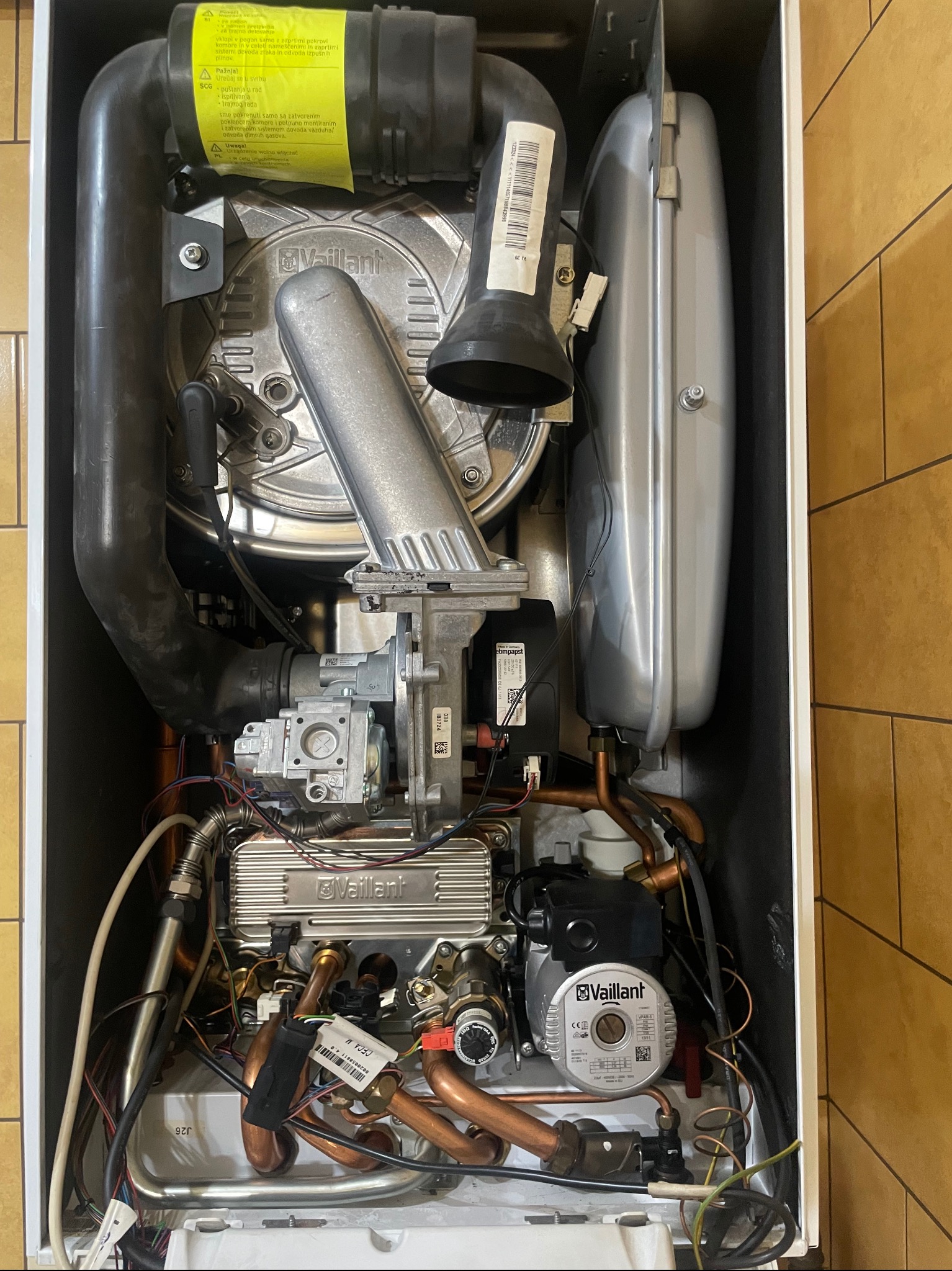 Wnętrze kotła gazowego Vaillant z widocznymi elementami instalacji, rurami miedzianymi i komponentami elektronicznymi. Detaliczny widok na podzespoły urządzenia.