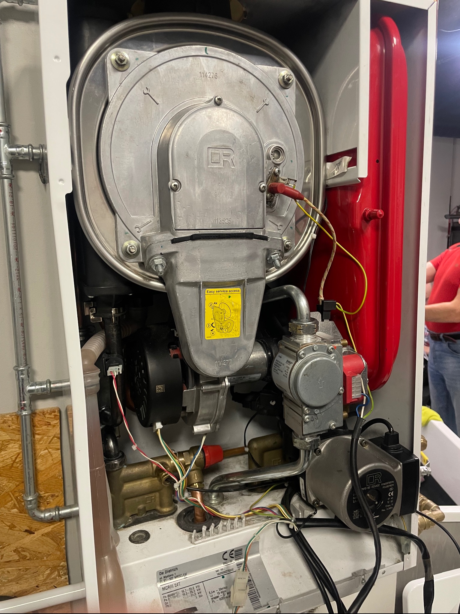Wnętrze kotła gazowego De Dietrich MCR/II 24T z widocznymi elementami instalacji i oznaczeniami producenta. Detaliczny widok na podzespoły w obudowie.