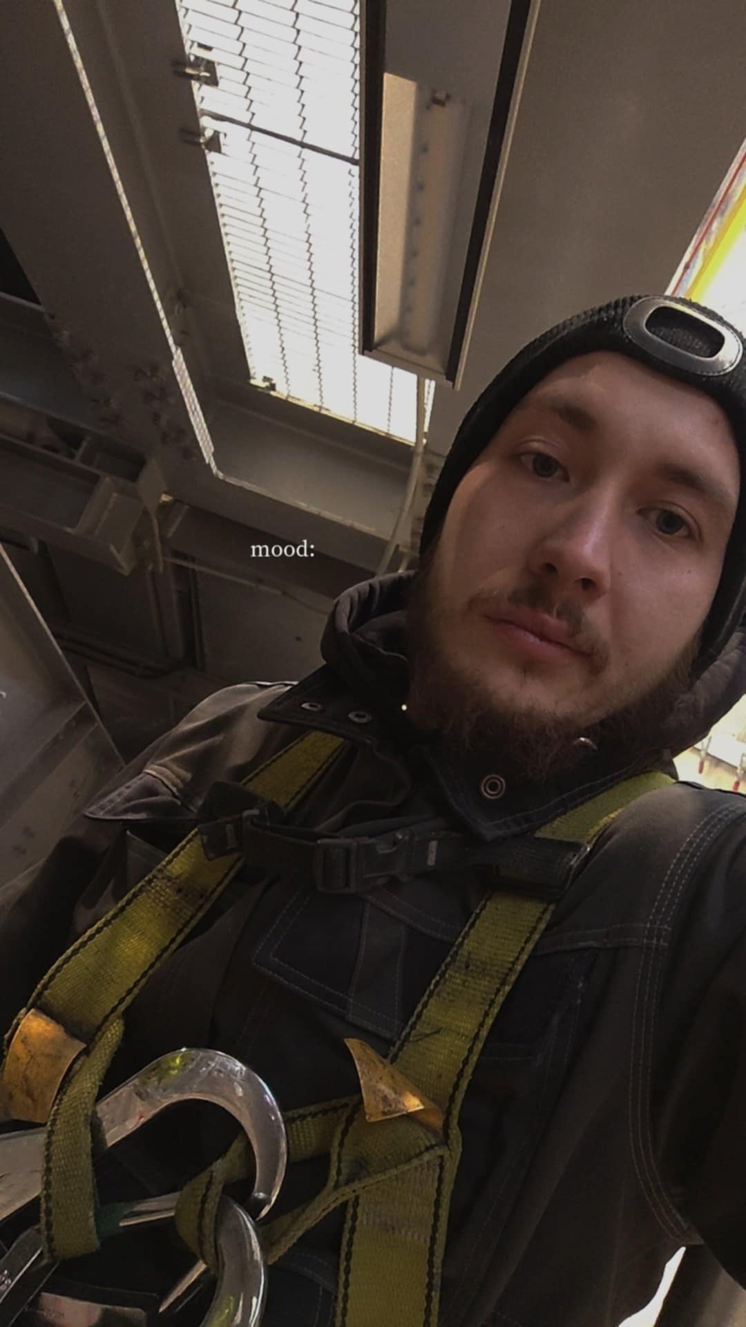 Selfie pracownika w uprzęży na tle konstrukcji stalowej hali. Widoczny fragment dachu z kratownicą. Ujęcie z dołu, podkreślające wysokość konstrukcji.