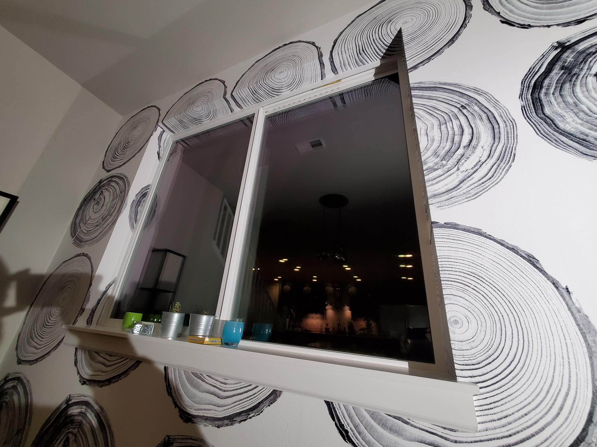 Ściana z tapetą imitującą przekrój pnia drzewa, okno z parapetem, na którym stoją dekoracje. Nietypowy wzór tapety, widok z dołu.