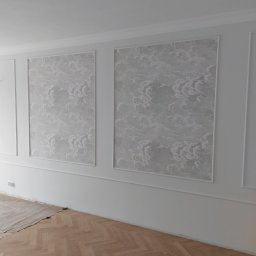 Viacheslav Dunda - Wykończone wnętrze: białe ściany z dekoracyjnymi panelami i wzorzystą tapetą w ramkach, parkiet w jodełkę. Częściowo zabezpieczona podłoga. Minimalistyczny design.