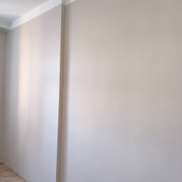 Viacheslav Dunda - Ściana w odcieniach beżu z białą listwą sufitową i przypodłogową. Widoczny fragment drewnianej podłogi. Gładka powierzchnia ściany po remoncie.