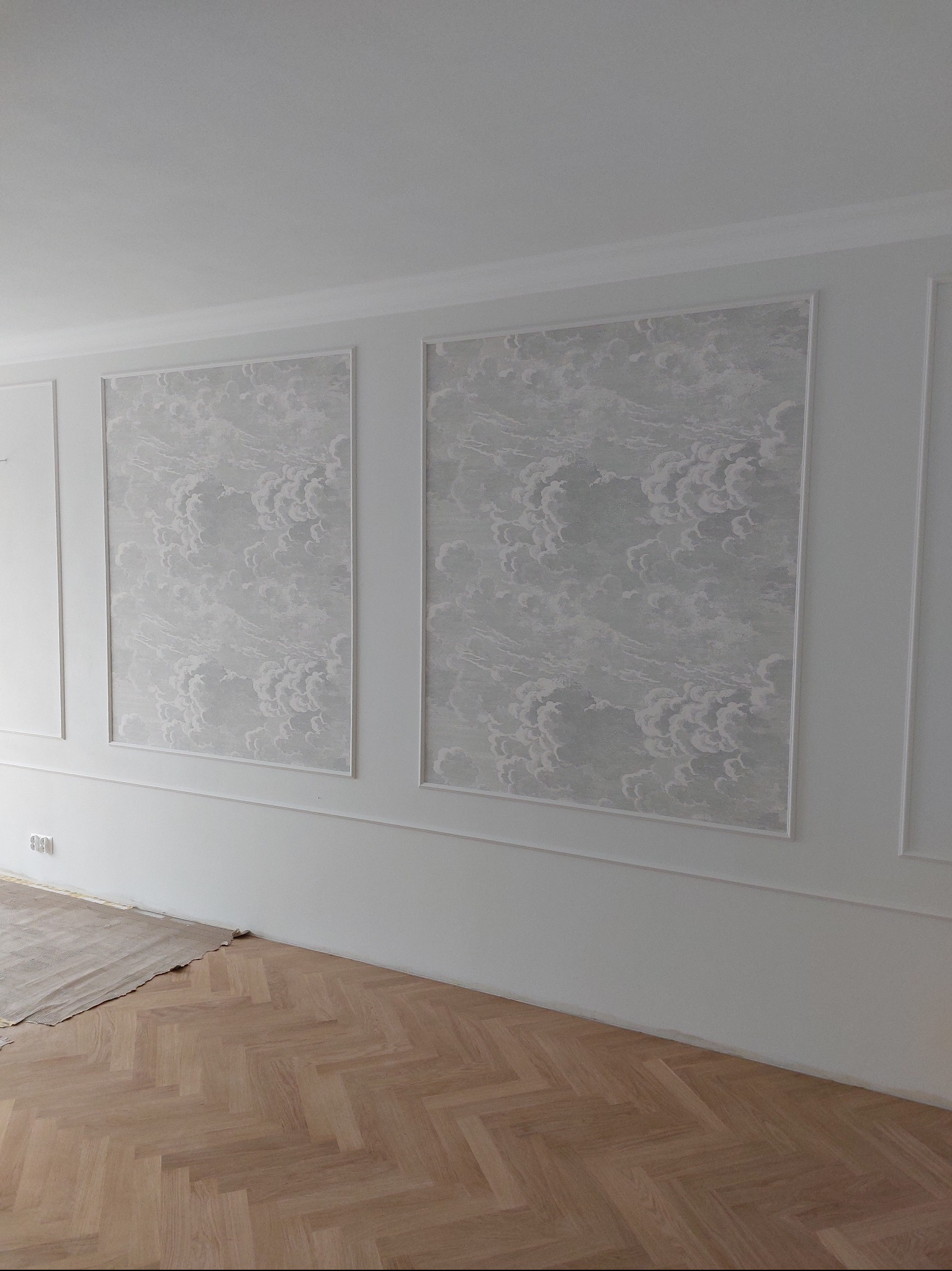 Wykończone wnętrze: białe ściany z dekoracyjnymi panelami i wzorzystą tapetą w ramkach, parkiet w jodełkę. Częściowo zabezpieczona podłoga. Minimalistyczny design.