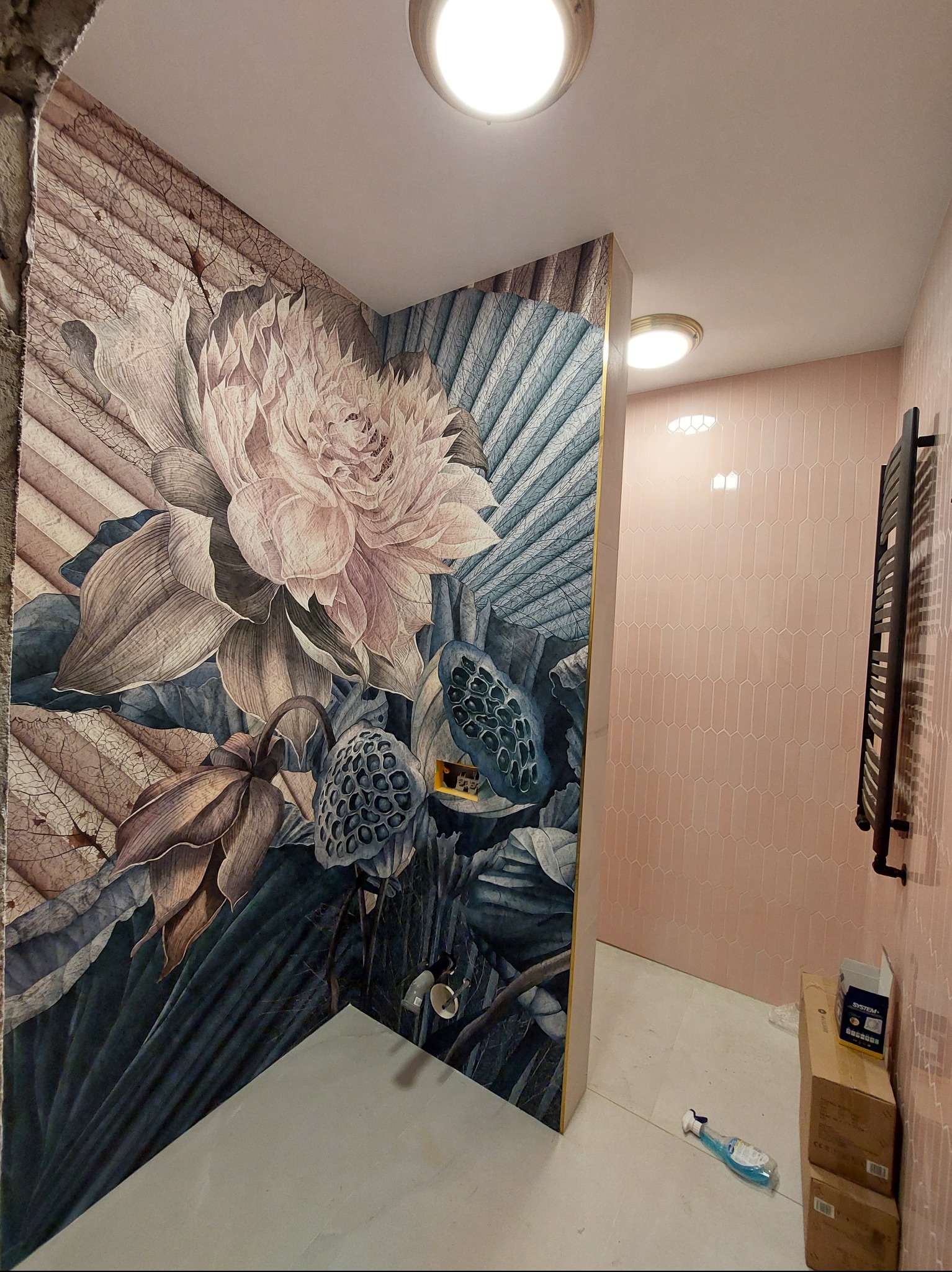 Wykończona łazienka z dekoracyjną, kwiatową tapetą na ścianie i różowymi, podłużnymi płytkami. Widoczny grzejnik drabinkowy i akcesoria do sprzątania.