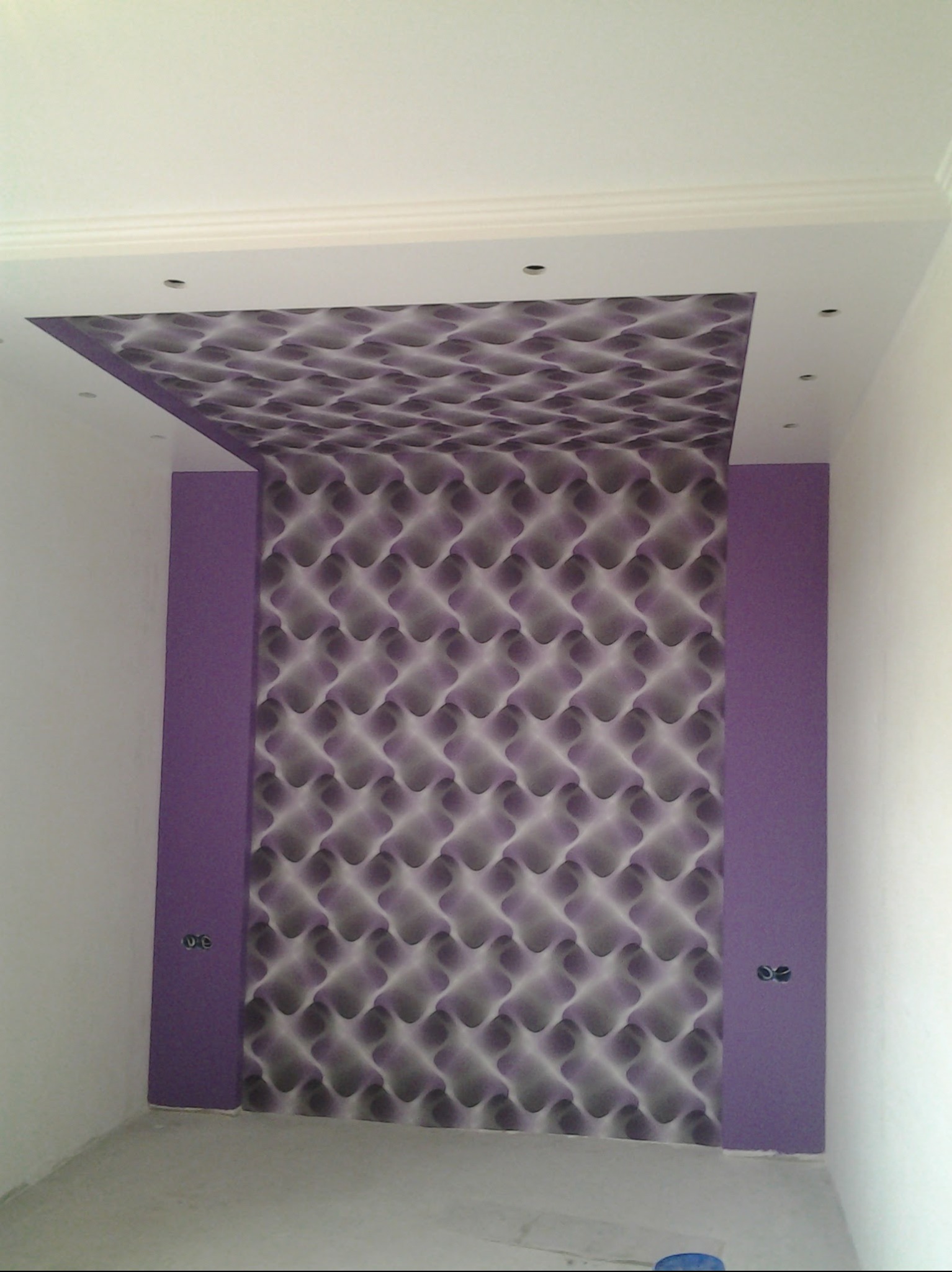 Pomieszczenie po remoncie: fioletowe pasy na ścianach, wzorzysta tapeta na suficie, białe ściany i listwy sufitowe. Widoczne gniazdka elektryczne.