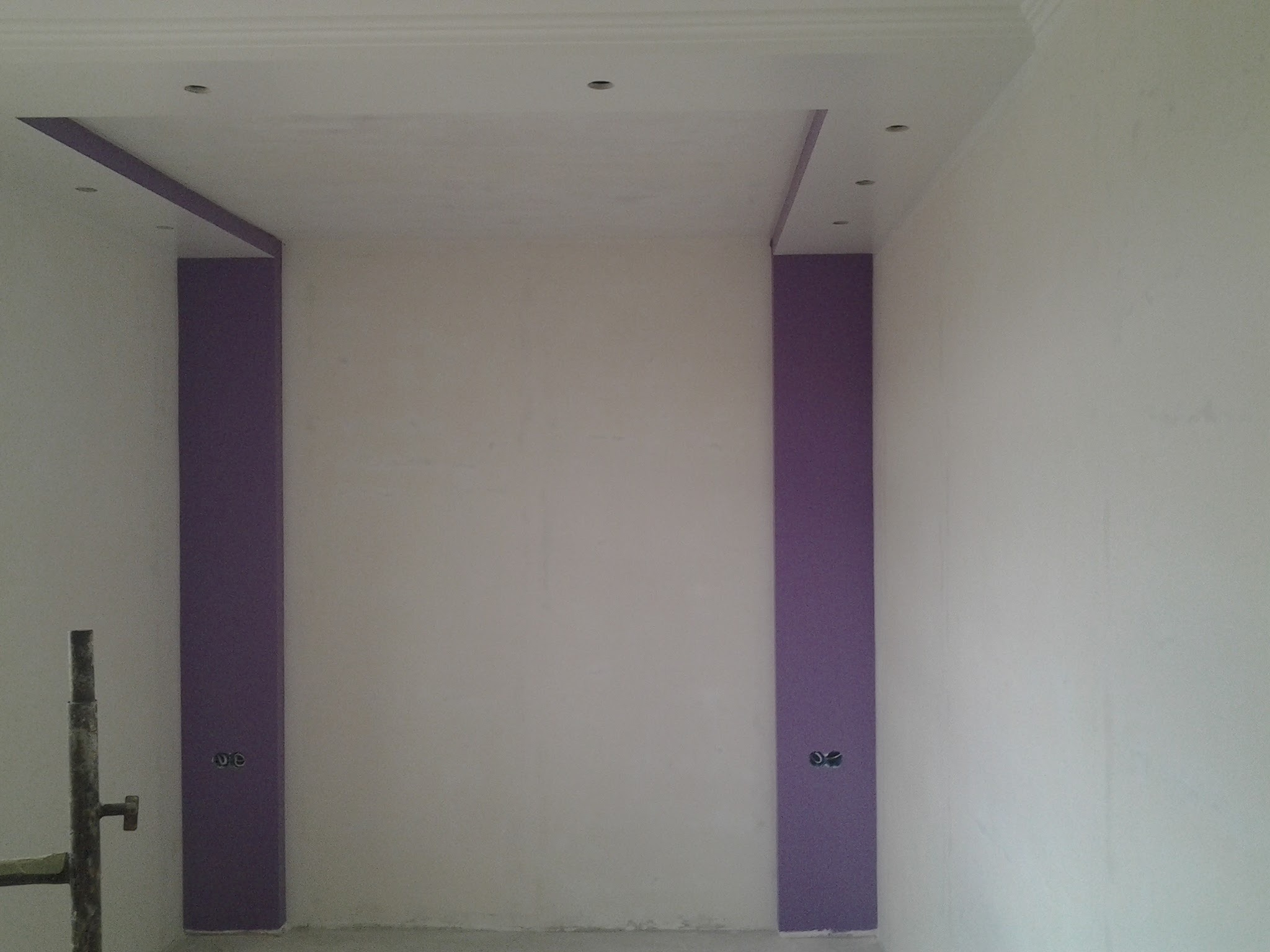 Wykończone wnętrze z dekoracyjnym malowaniem ścian w odcieniach bieli i fioletu. Widoczne gniazdka elektryczne i fragment rusztowania.