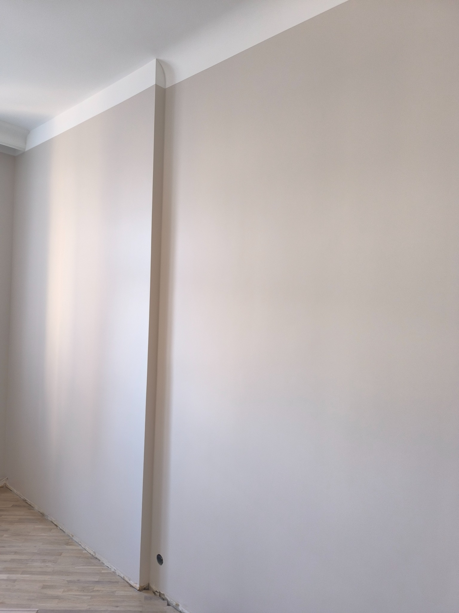 Ściana w odcieniach beżu z białą listwą sufitową i przypodłogową. Widoczny fragment drewnianej podłogi. Gładka powierzchnia ściany po remoncie.
