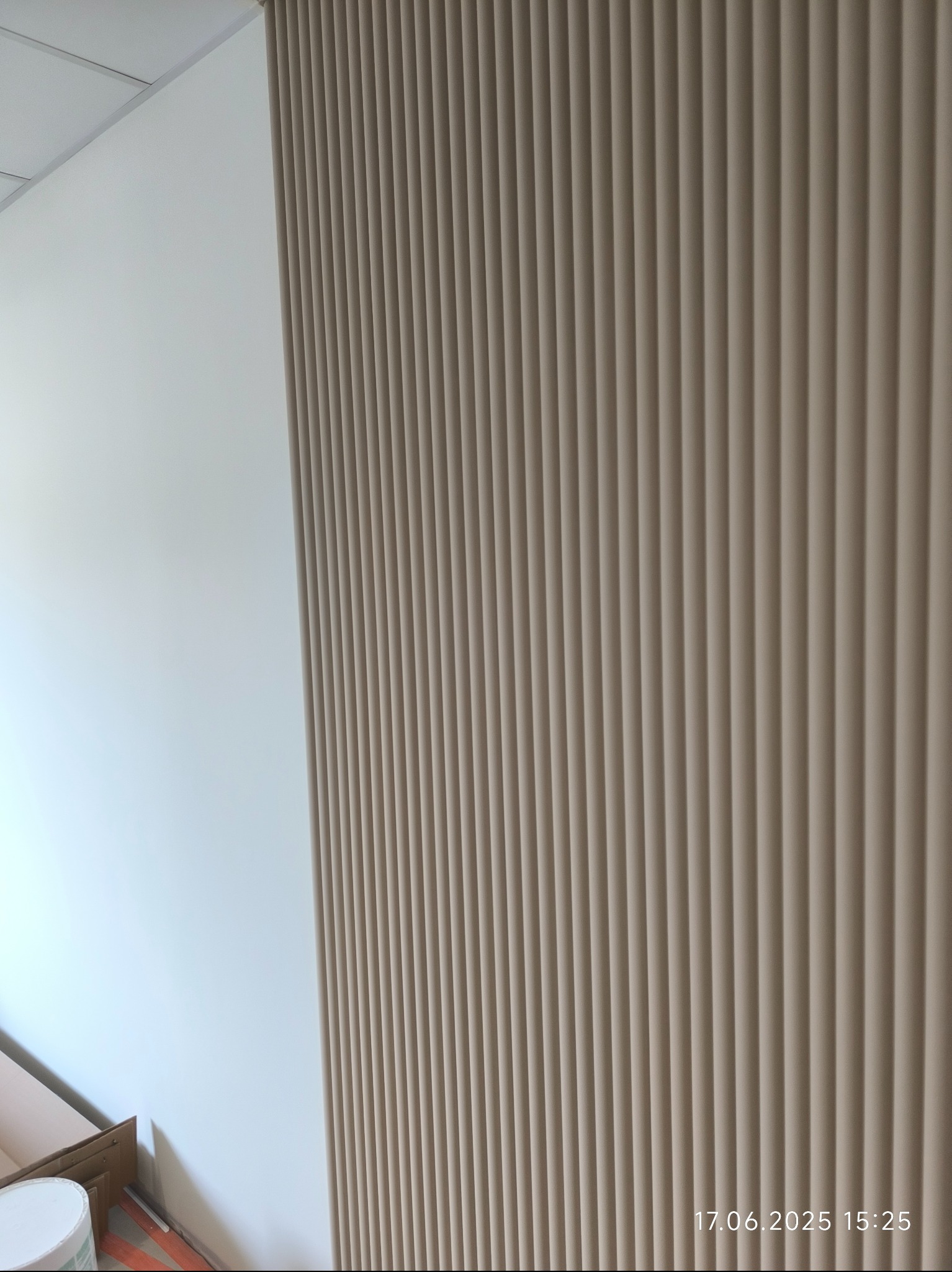 Wykończona ściana z dekoracyjnymi, pionowymi panelami w odcieniach beżu, przylegająca do gładkiej, białej ściany. Widoczne detale wykończenia i fragment podłogi.