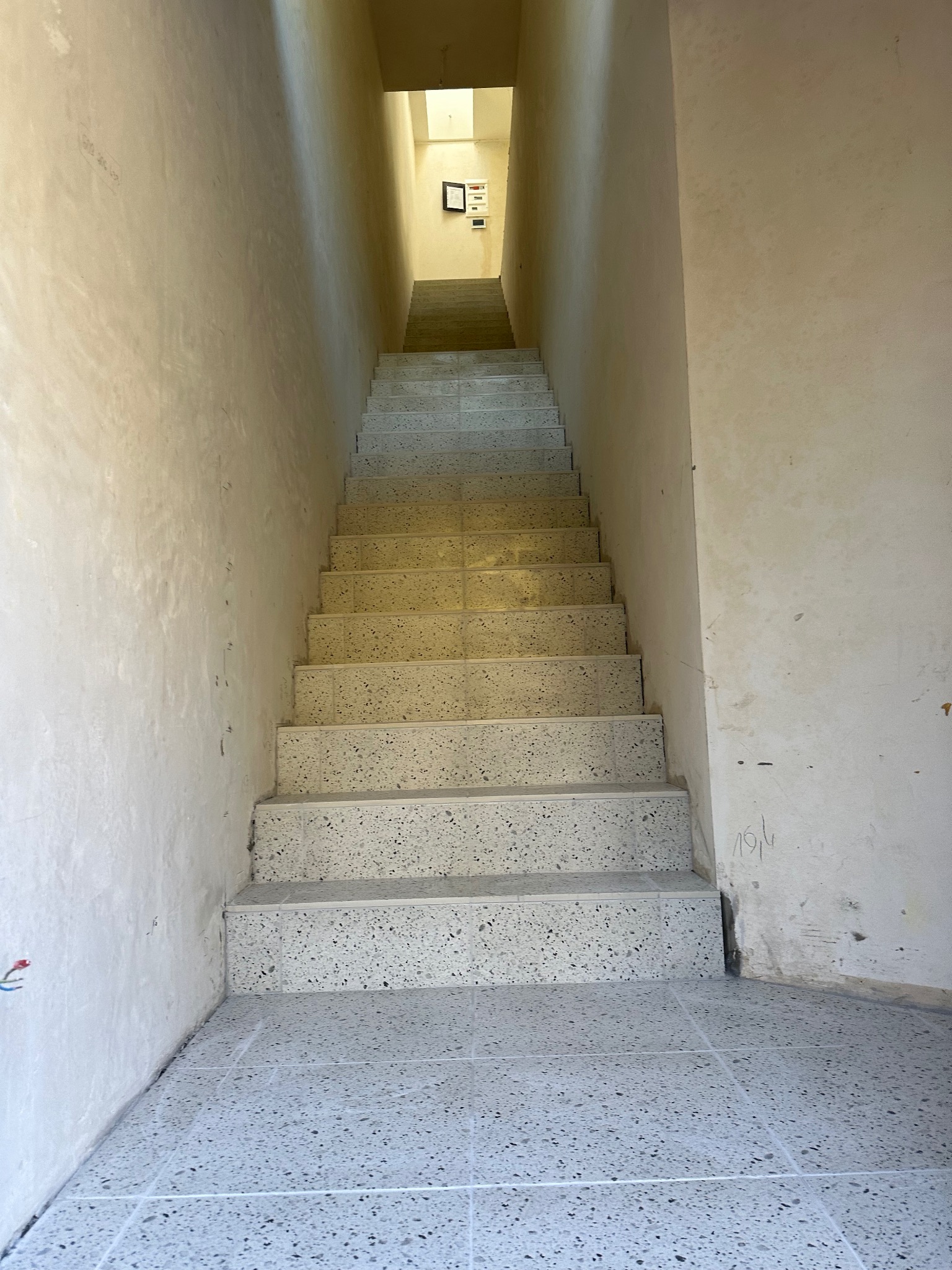 Wykończone schody z terazzo prowadzące w górę, ściany w jasnym odcieniu beżu, widoczne ślady po pracach wykończeniowych.