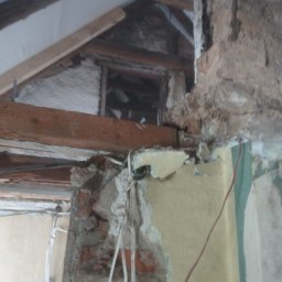 Mann sp. z o.o. - Demontaż ściany działowej w trakcie remontu poddasza. Widoczne odsłonięte cegły, fragmenty instalacji elektrycznej i drewniana konstrukcja dachu.