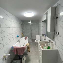 Mann sp. z o.o. - Remont łazienki w trakcie: białe marmurowe płytki, wolnostojąca wanna na srebrnych nóżkach, biała szafka z umywalką, toaleta. Widoczne narzędzia i materiały budowlane.