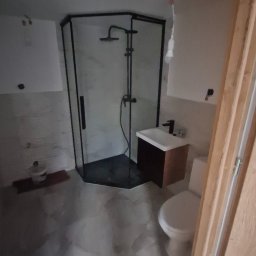 Mann sp. z o.o. - Nowoczesna kabina prysznicowa z czarnymi profilami, umywalka z szafką i toaleta w wyremontowanej łazience. Widoczne niedoskonałości wykończenia.