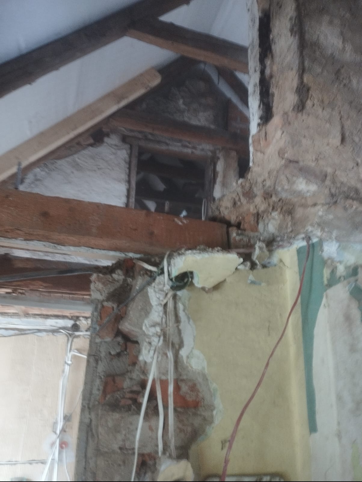 Demontaż ściany działowej w trakcie remontu poddasza. Widoczne odsłonięte cegły, fragmenty instalacji elektrycznej i drewniana konstrukcja dachu.