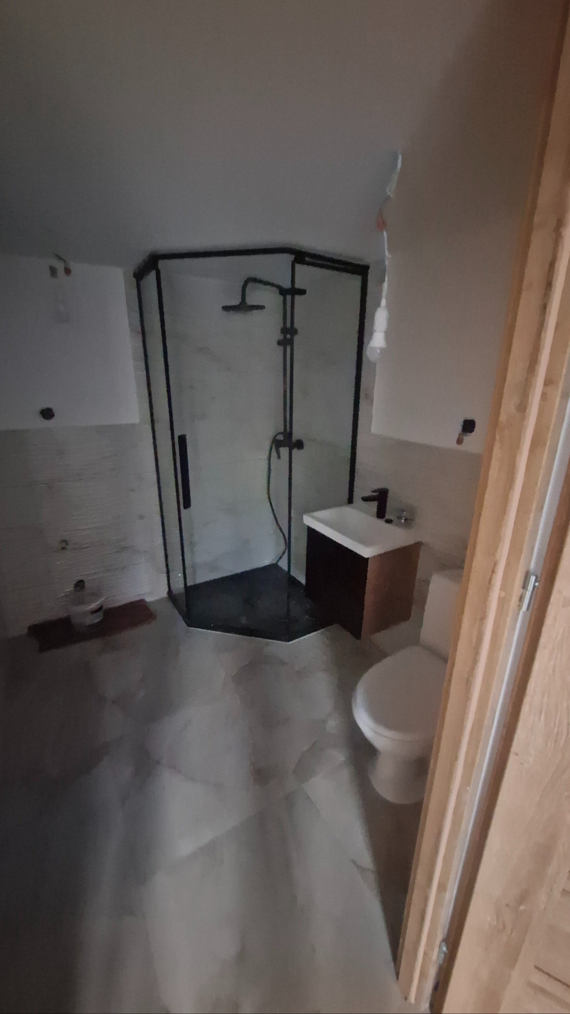 Nowoczesna kabina prysznicowa z czarnymi profilami, umywalka z szafką i toaleta w wyremontowanej łazience. Widoczne niedoskonałości wykończenia.