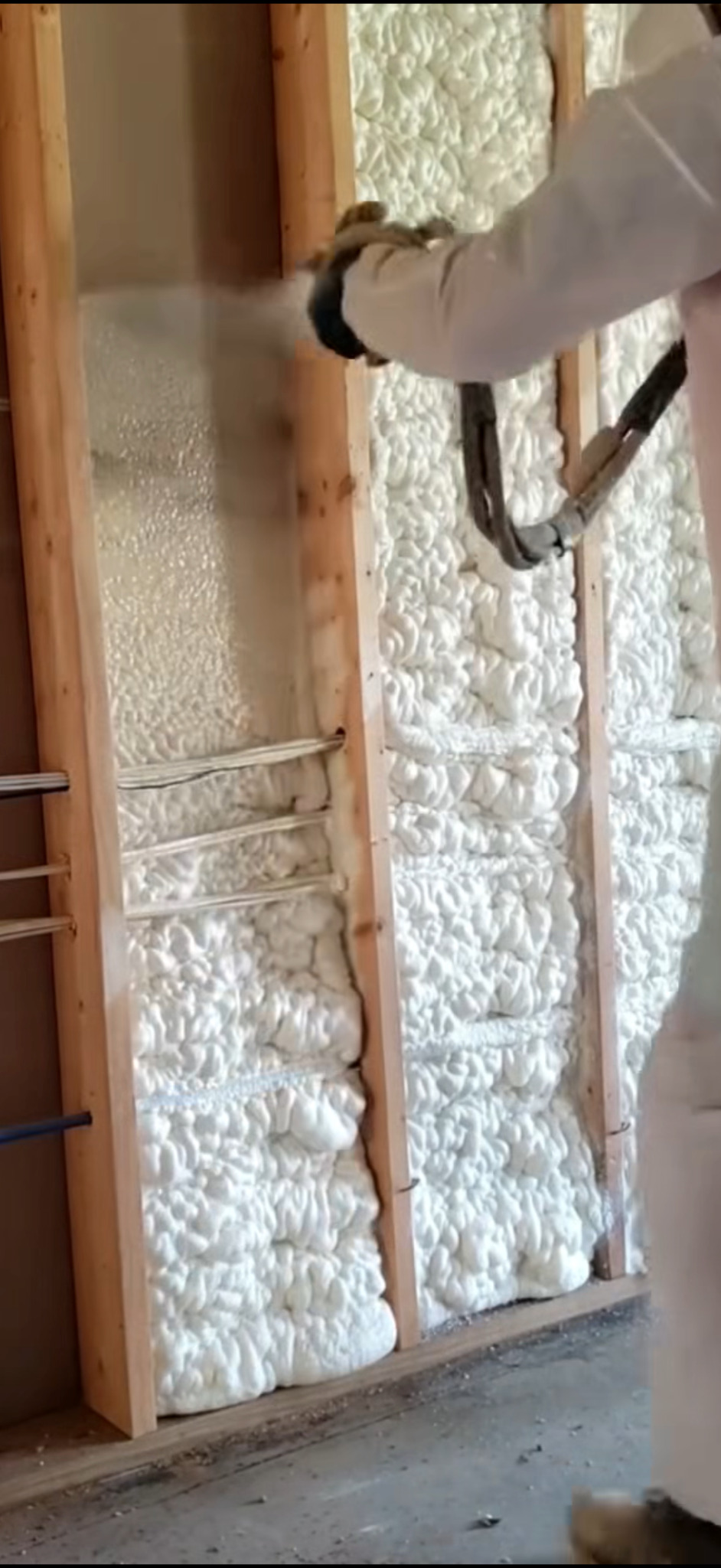 Aplikacja pianki PUR na ścianę w trakcie ocieplania. Widoczne drewniane elementy konstrukcyjne i instalacja. Izolacja termiczna i akustyczna w trakcie realizacji.