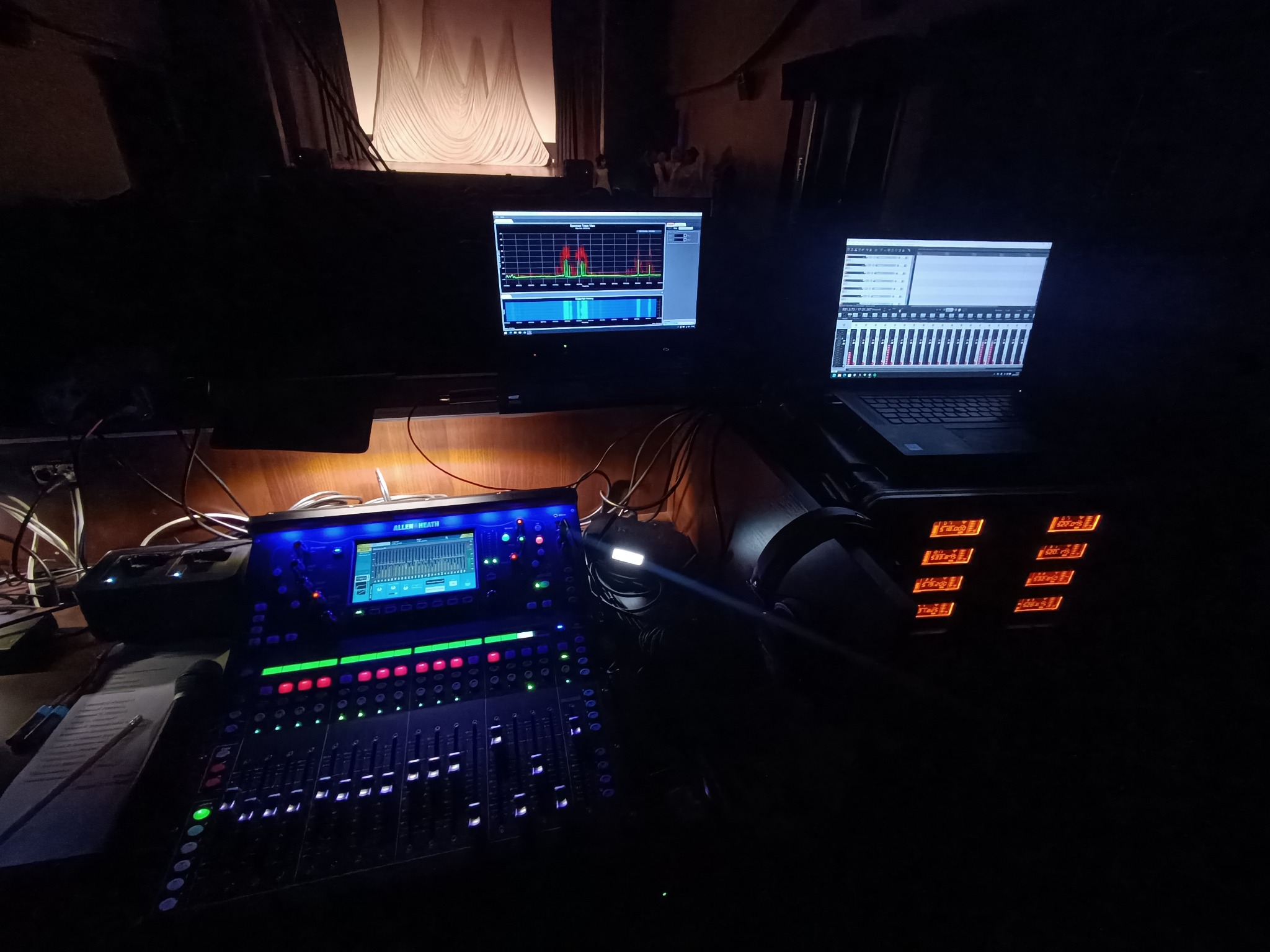 Panel mikserski Allen&Heath z podłączonym laptopem i monitorem, widoczne wskaźniki poziomów dźwięku, ustawione na scenie w ciemnym otoczeniu.