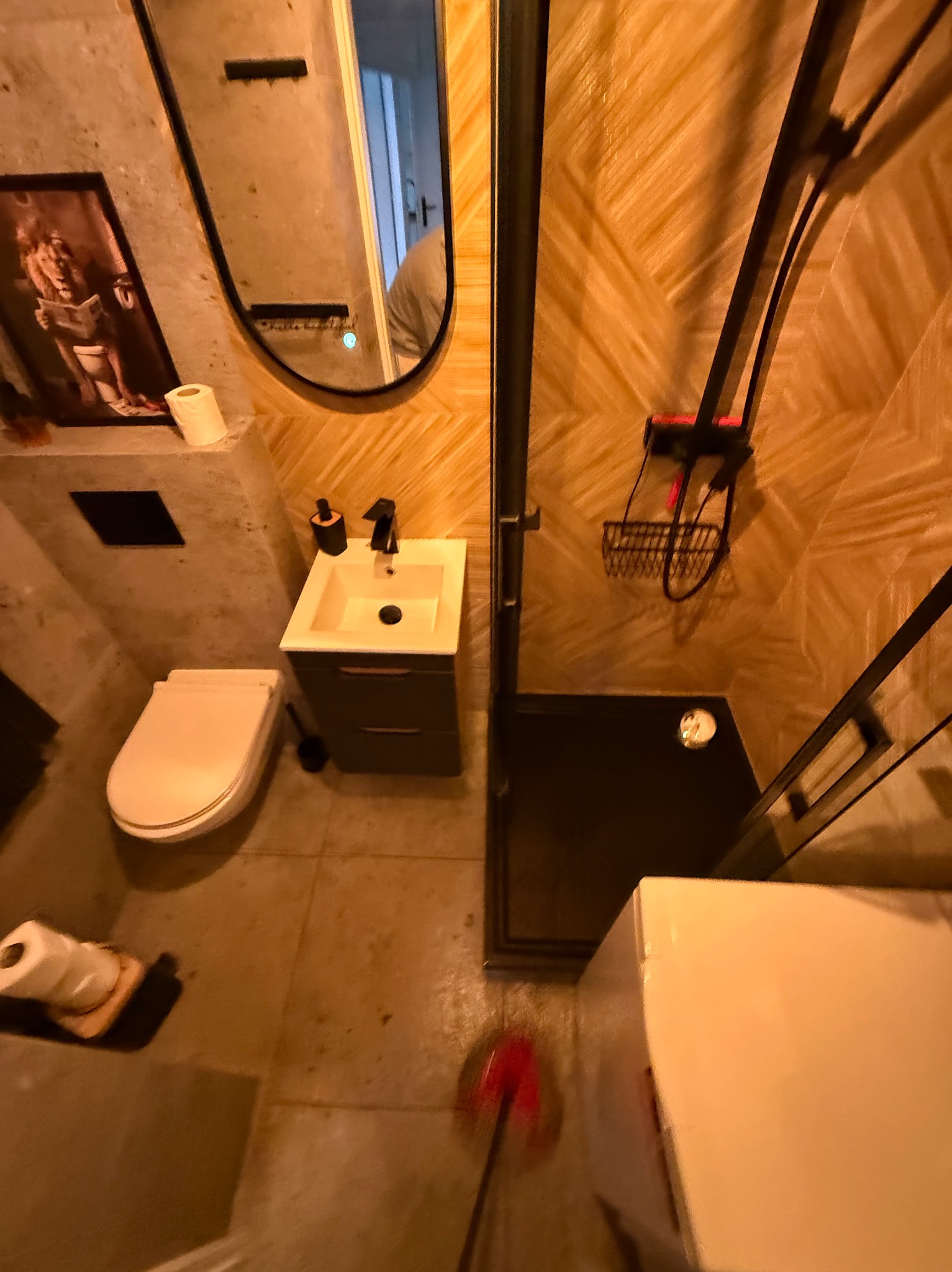 Nowoczesna łazienka z kabiną prysznicową typu walk-in, umywalką z szafką i toaletą. Na ścianie lustro i obrazek. Widoczny mop do podłogi.