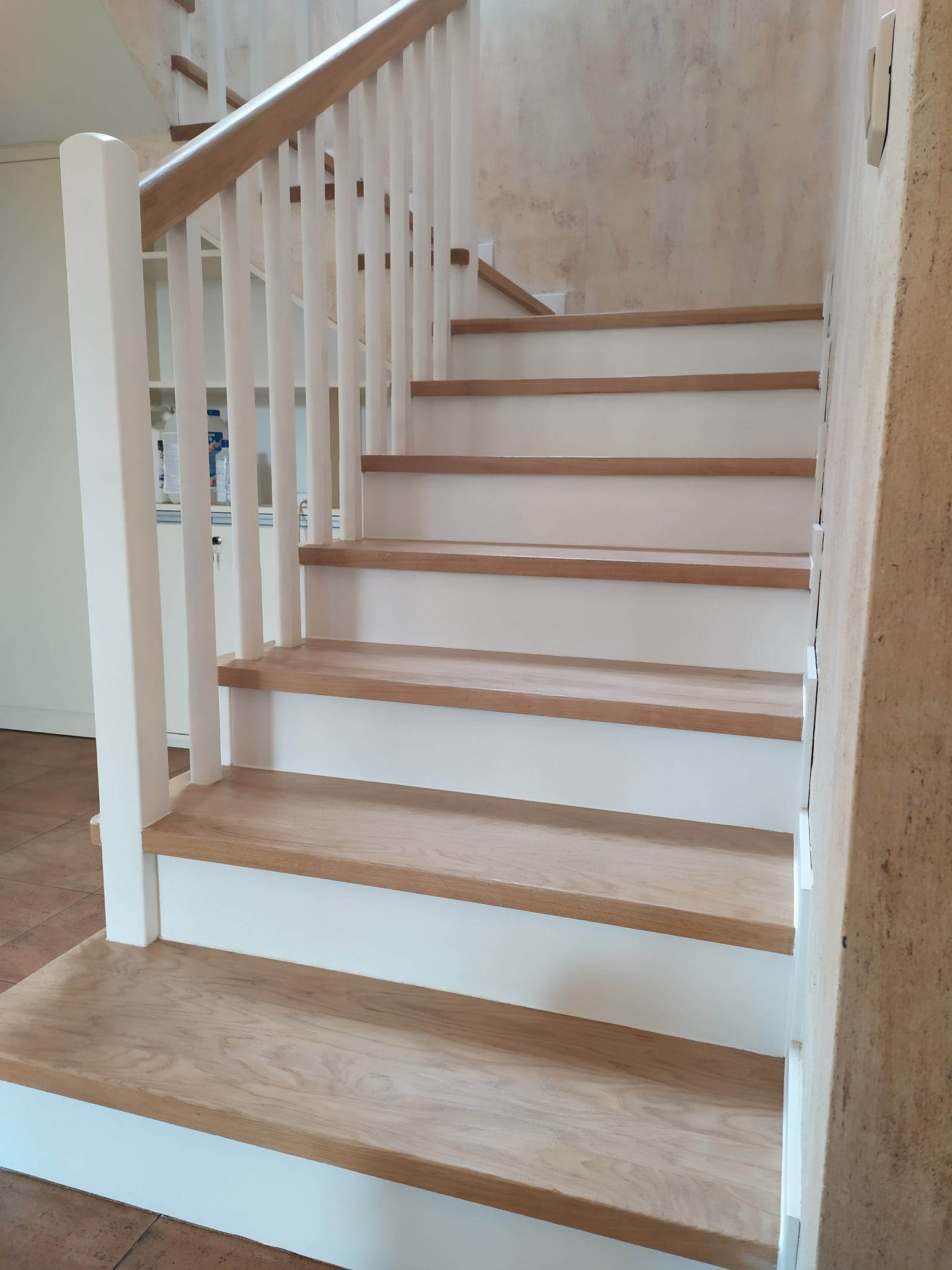 Jasne, drewniane schody z białymi podstopnicami i balustradą. Widoczne detale wykończenia i naturalna tekstura drewna. Ujęcie od dołu, podkreślające perspektywę.