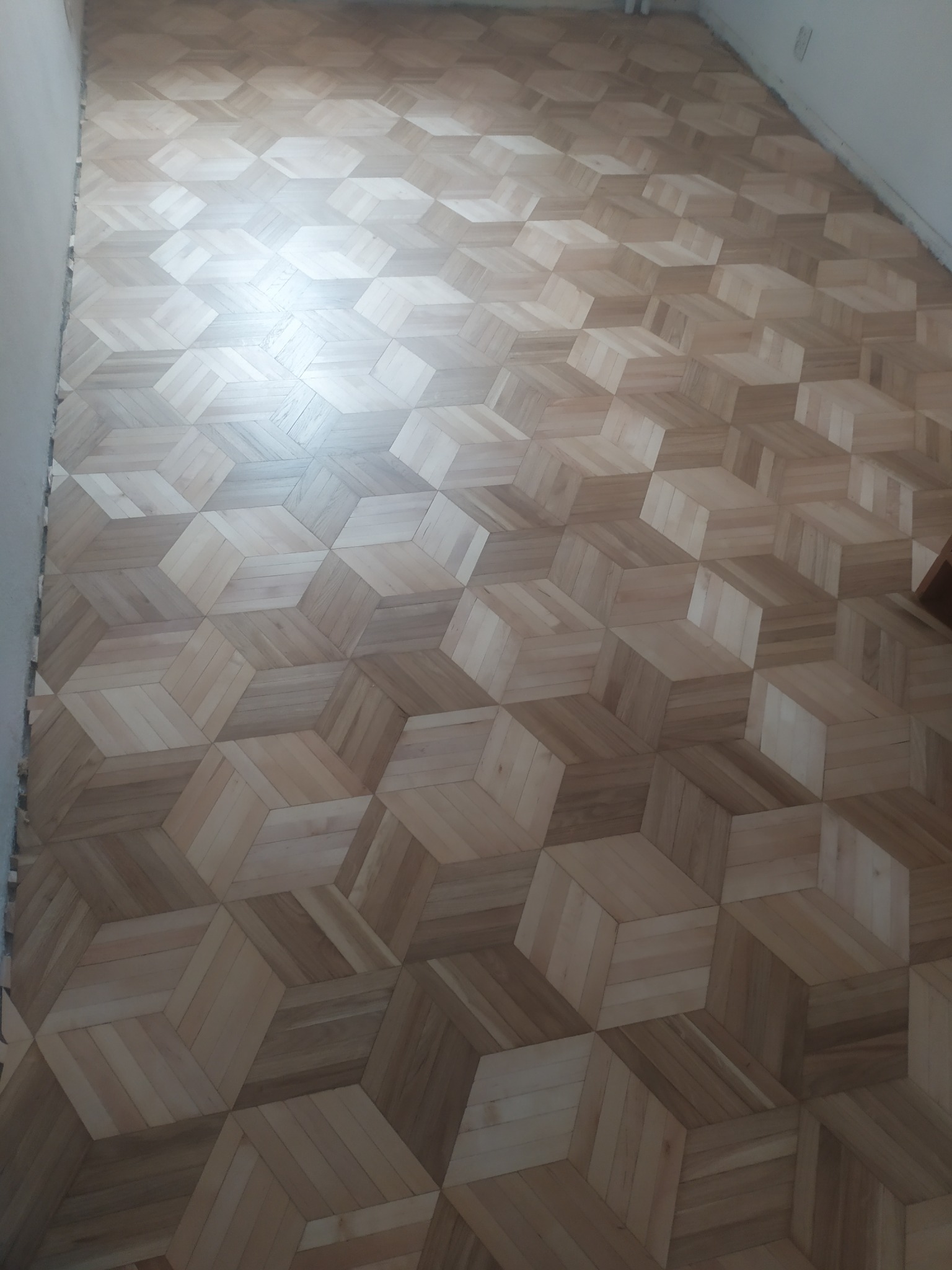 Ułożony parkiet w geometryczny wzór 3D, jasne drewno, widok z góry, świeżo po montażu, delikatne światło podkreśla strukturę drewna.