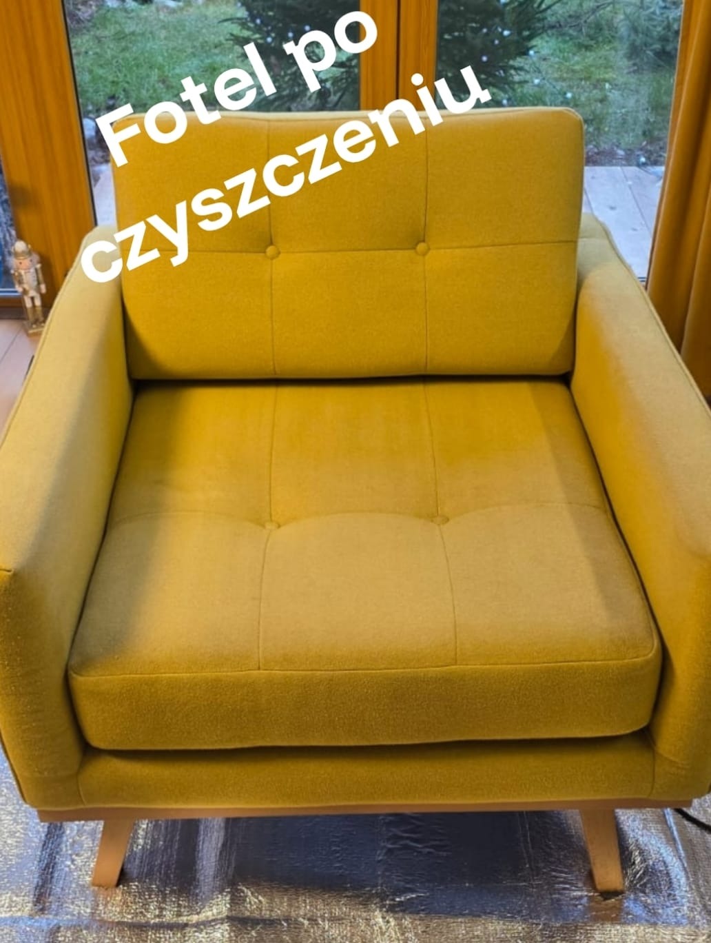 Żółty fotel tapicerowany z guzikami po czyszczeniu, ustawiony na folii ochronnej. Widoczne drewniane nóżki i fragment okna w tle.