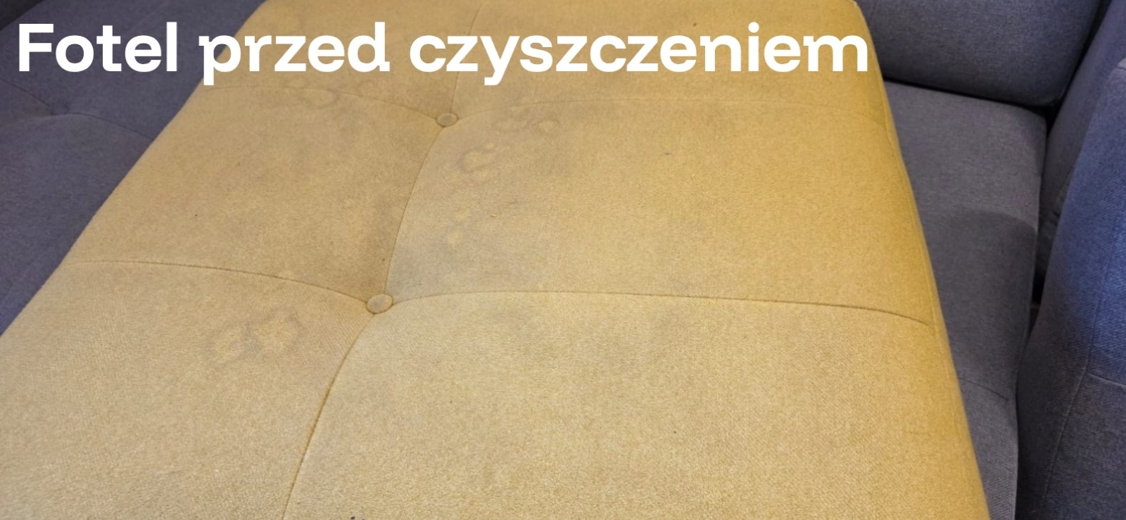 Beżowy fotel z widocznymi plamami na tapicerce, stan przed czyszczeniem. Widoczny fragment szarej sofy w tle. Ujęcie z bliska, ukazujące detale zabrudzeń.