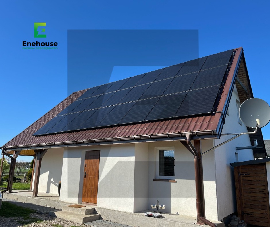 Dom jednorodzinny z brązowym dachem, na którym zamontowano czarne panele słoneczne. Błękitne niebo w tle. Widoczna antena satelitarna.