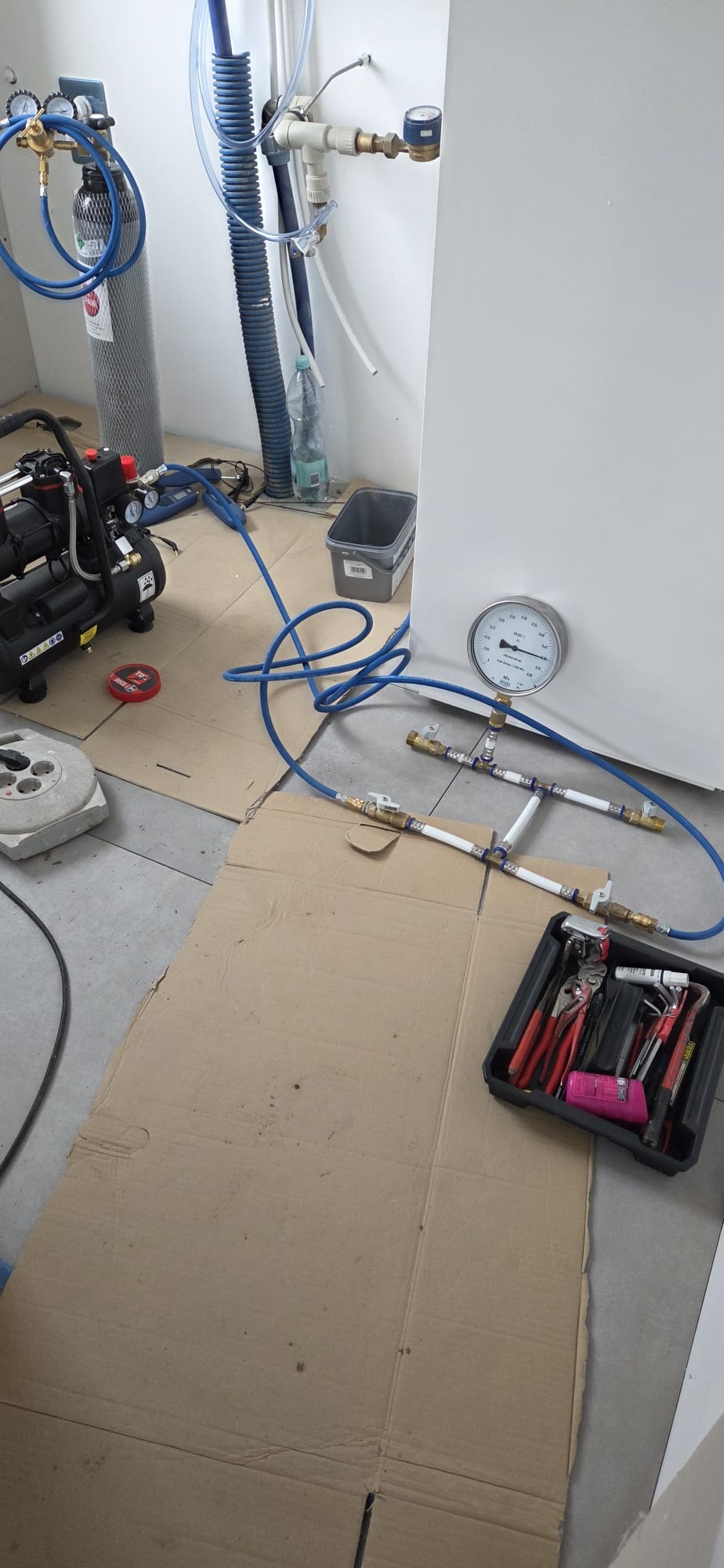 Instalacja wodna z manometrem i narzędziami w Krakowie. Widoczny kompresor i skrzynka z narzędziami. Prace hydrauliczne w trakcie realizacji.