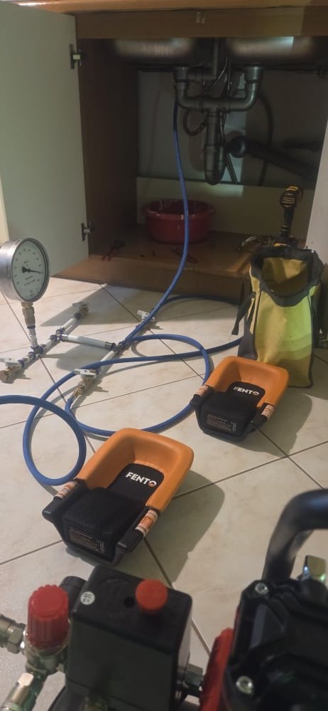 Udrażnianie zlewu: narzędzia Fento, manometr i wąż pod szafką zlewozmywakową. Widoczny syfon i instalacja wodna. Praca w toku.