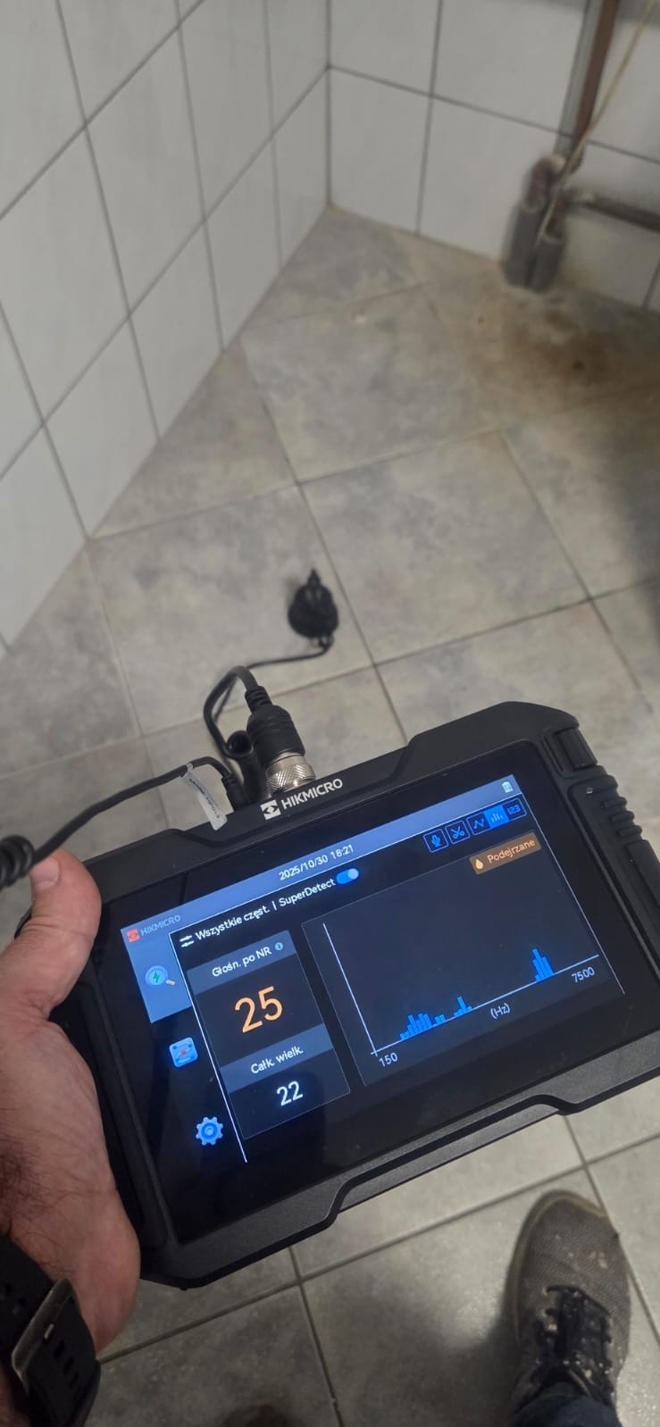 Diagnostyka rur: urządzenie HIKMICRO z ekranem wskazującym parametry dźwiękowe w pomieszczeniu z płytkami. Analiza akustyczna instalacji wodnej.