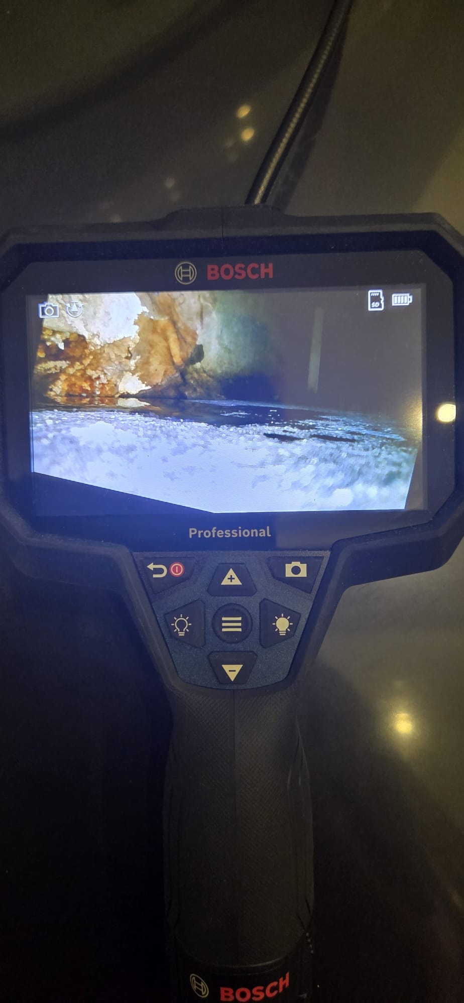 Kamera inspekcyjna Bosch Professional pokazuje wnętrze zardzewiałej rury, prawdopodobnie podczas udrażniania. Widoczne przyciski sterujące i logo Bosch.