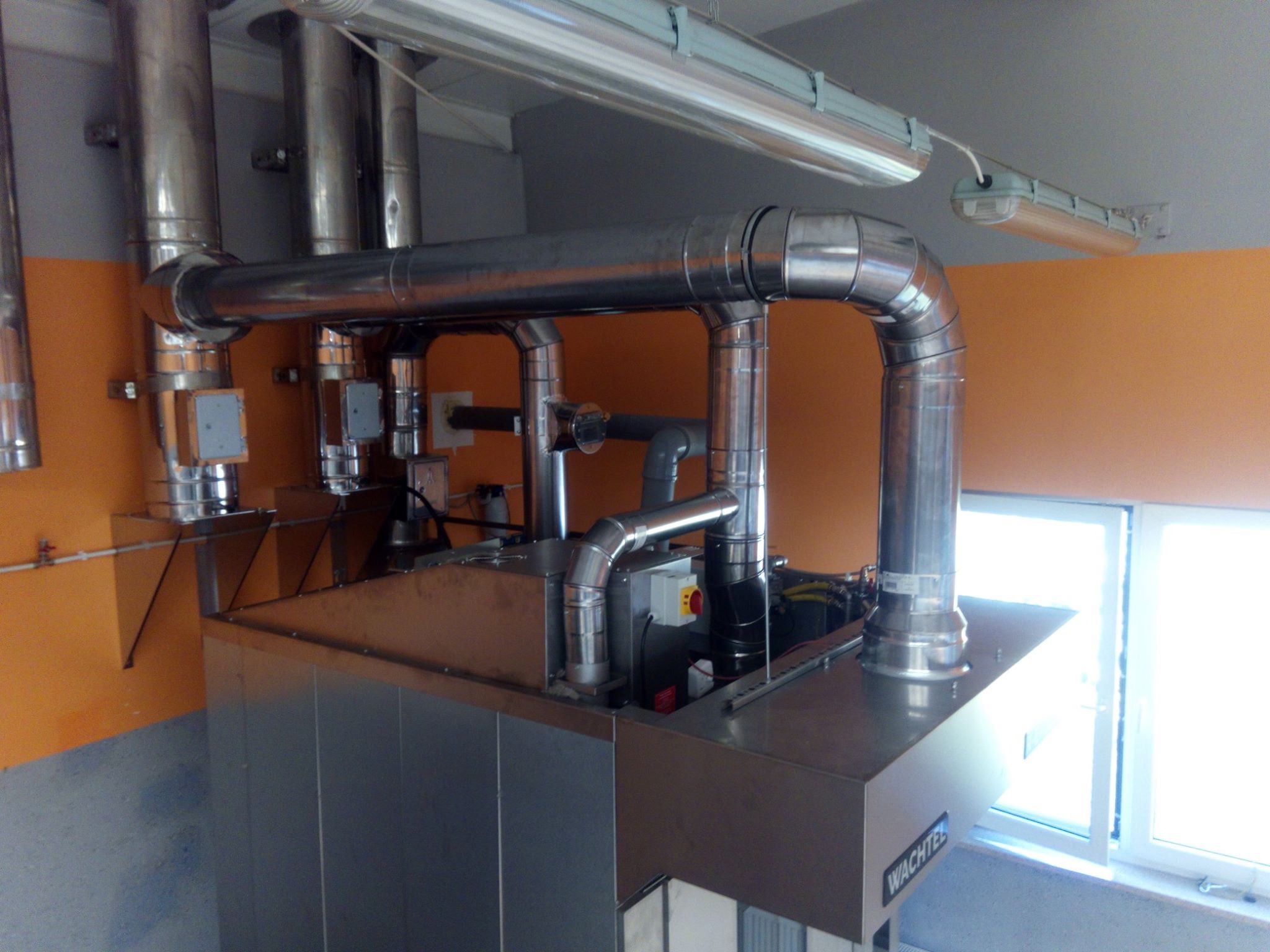 Kompletna instalacja rekuperacji z rurami wentylacyjnymi w budynku, Częstochowa. Widoczne elementy sterujące i okno w tle. Metalowe wykończenie.