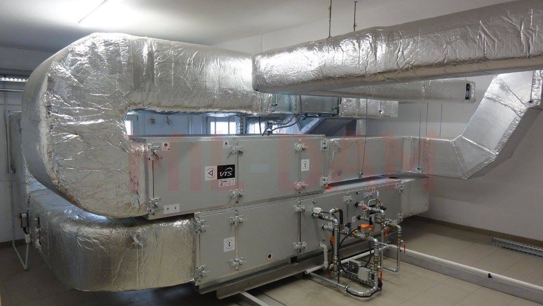 Rozbudowana instalacja wentylacyjna z izolowanymi kanałami i centralą VTS w pomieszczeniu technicznym. Widoczne liczne rury i zawory.