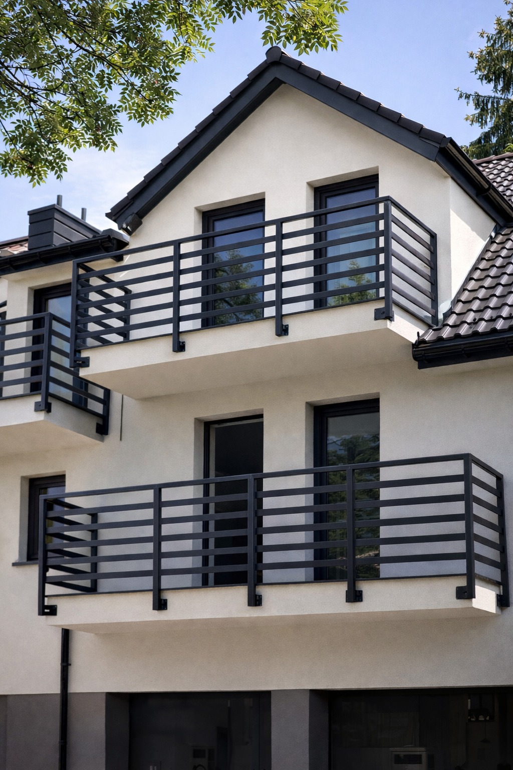 Dwukondygnacyjny dom z balkonami zabezpieczonymi czarnymi, poziomymi balustradami. Minimalistyczny design, jasna elewacja, ciemna stolarka okienna i dach.
