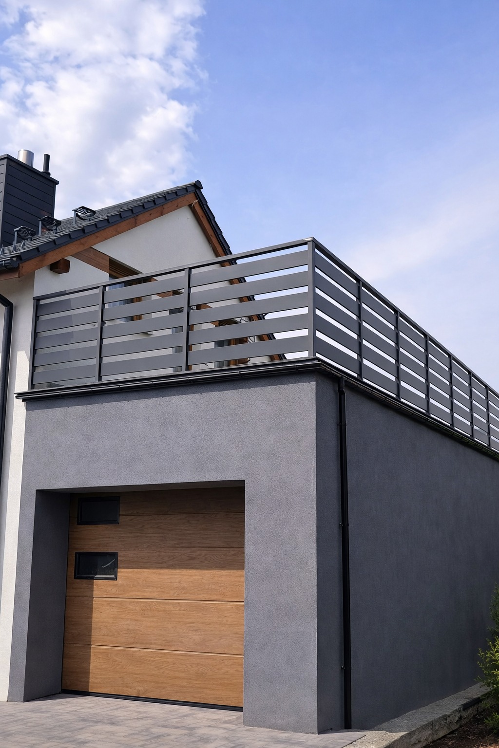 Szara, pozioma balustrada na dachu garażu przylegającego do domu jednorodzinnego. Widok z dołu, błękitne niebo w tle. Nowoczesny design.