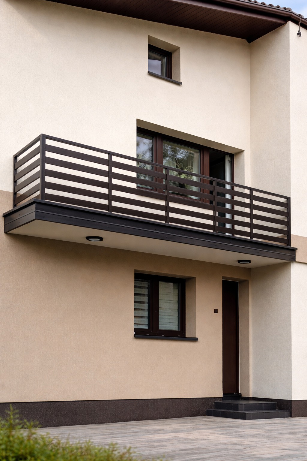 Nowoczesna balustrada balkonowa z poziomych, ciemnych desek na tle elewacji domu w beżach i brązach. Widok z dołu, podkreślający minimalistyczny design.